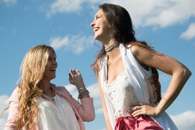 Low angle view of young women laughing while looking away against sky