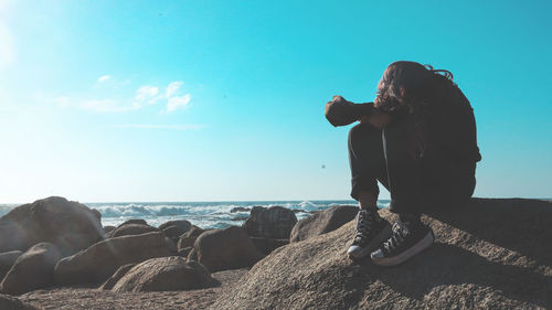 Rear view of man standing on rock by sea against sky