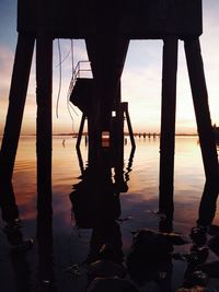 Silhouette built structure on beach against sky during sunset