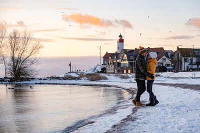 Rear view of man standing on snow against sky during sunset