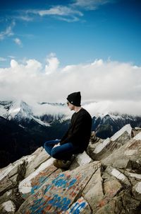 Man sitting on mountain against sky