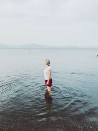 Rear view of woman standing in sea against sky