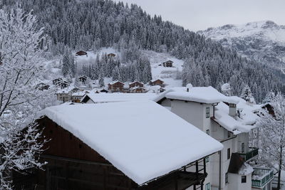 Snow covered houses by trees and buildings against sky