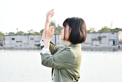 Side view of woman gesturing against river and sky