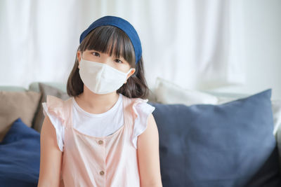 Portrait of cute girl wearing mask sitting on sofa at home