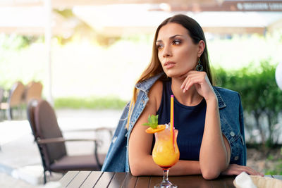 Young woman with drink sitting at sidewalk cafe