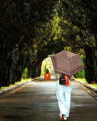 Rear view of woman carrying umbrella while walking on footpath