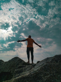 Rear view of man standing on rock against sky
