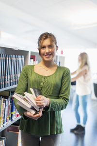 Portrait of happy teenage girl holding books in school library