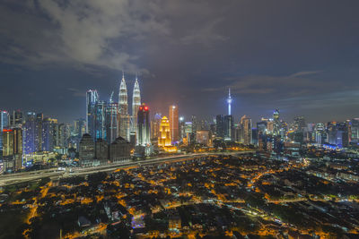 Illuminated buildings in city against cloudy sky