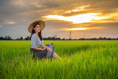 Side view of thoughtful woman sitting on land against sky during sunset