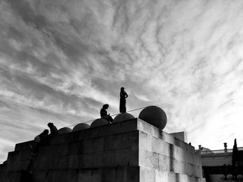 Low angle view of silhouette statue by historic building against sky