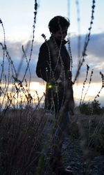 Woman standing on field against sky during sunset