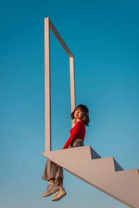 Low angle view of boy standing against blue sky