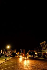 Illuminated street by buildings against sky at night