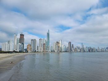 Buildings by river against cloudy sky