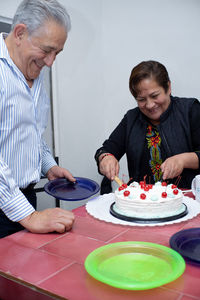 An older man with his friends celebrating a birthday, handing out the cake at an indoor party.