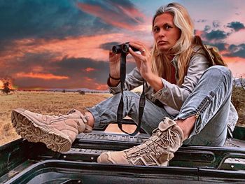 Young woman photographing while sitting against sky