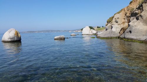 Rocks in sea against clear blue sky