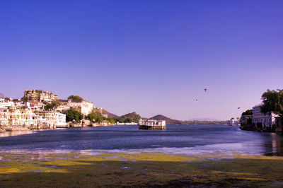 Buildings by sea against clear blue sky