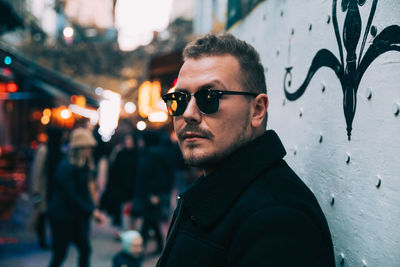 Portrait of young man wearing sunglasses standing against wall