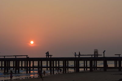 Silhouette people on beach against clear sky during sunset