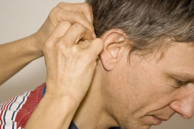 Cropped hands of doctor inserting acupuncture needle behind man ear