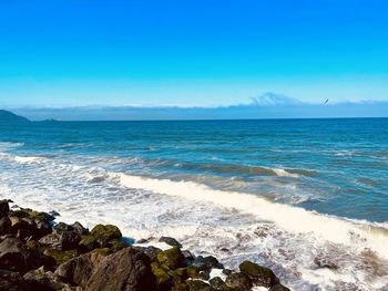 Scenic view of sea against blue sky and waves crashing off the rocks