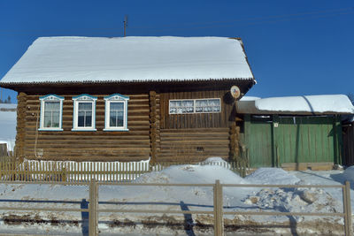 House on snow covered field by building against sky