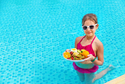Smiling girl holding plate of fruits in swimming pool