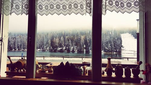 Trees on snow covered field seen through window