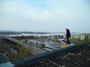 Man standing on railing by sea against sky