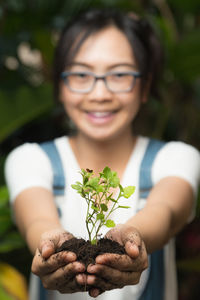 Portrait of smiling girl holding plant in greenhouse
