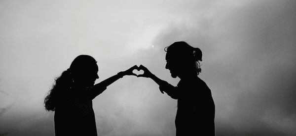 Silhouette couple making heart shape standing against sky