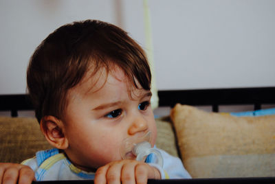 Close-up of baby boy with pacifier in mouth looking away at home