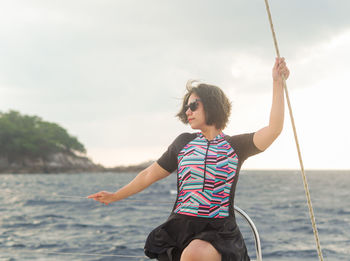 Side view of woman sitting on swing at beach against sky