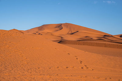 Footsteps with sand dunes in desert on sunny summer day against clear sky