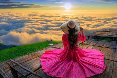 Rear view of woman with umbrella against sky during sunset