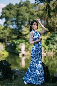 Portrait of young woman with arms raised standing against lake