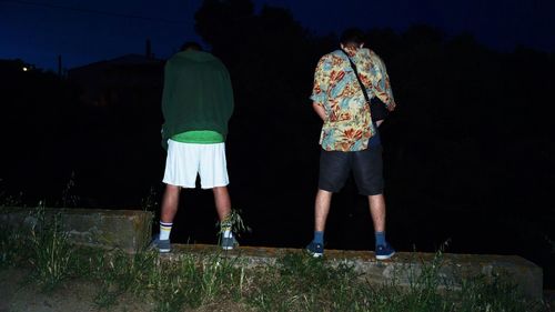 Rear view of man standing on landscape against sky at night