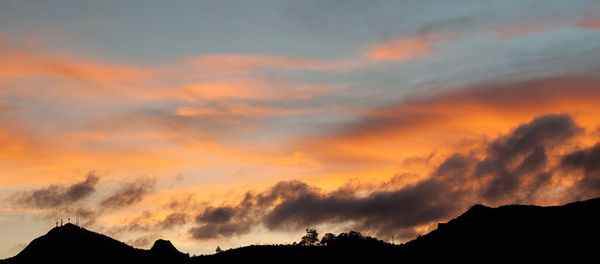 Silhouette trees against dramatic sky during sunset