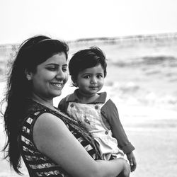 Smiling mother carrying daughter at beach