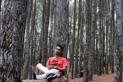 Portrait of smiling man sitting on tree trunk in forest