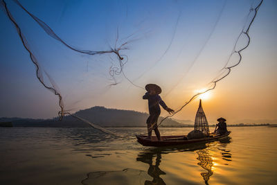 Man fishing in lake against sky during sunset