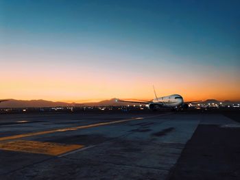 Airplane on airport runway against sky during sunset