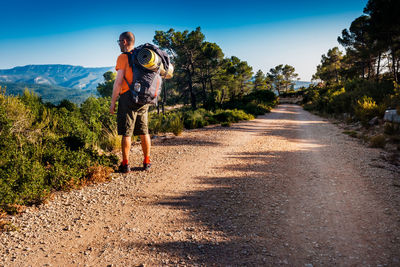 Side view of man with backpack standing on dirt road