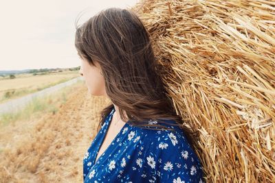 Side view of young woman leaning on hay bale