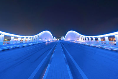 Illuminated bridge against blue sky at night