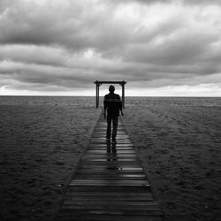 Rear view of man standing on beach against sky