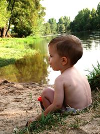 Shirtless boy sitting by lake